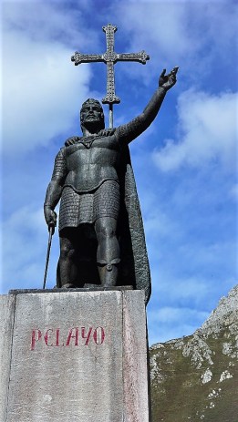 Het standbeeld van Don Pelayo, eerste koning van Asturias. Het beeld staat op een zeer hoge sokkel waarop in rode letter Pelayo staat. Pelayo staat in zijn maliënkolder, mantel en helm, met de linkerhand geheven en in de rechter draagt hij zijn zwaard. Achter hem staat het Cruz de la Victoria.